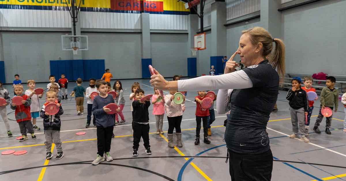 Woman demonstrates how to hold a disc to a group of young kids