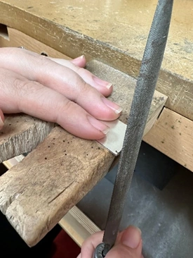 fingers holding a piece of sterling silver with the edge being filed