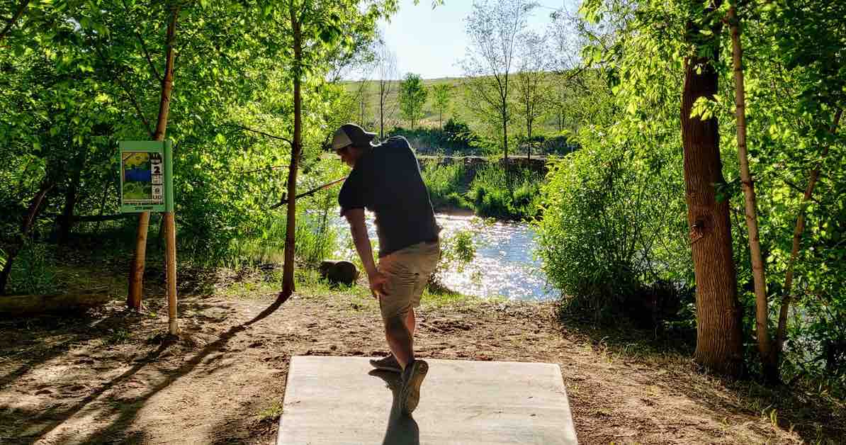 A young man throwing a disc in a wooded area over a river