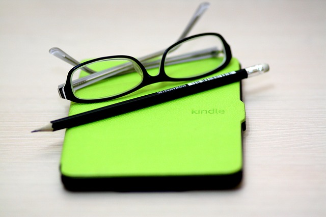 glasses and pencil sitting on top of kindle in green case