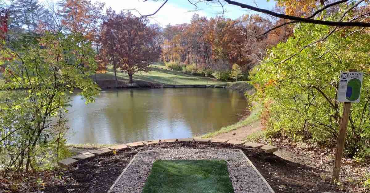Turf tee pad leads to water carry and well-manicured green beyond surrounded by trees in fall red