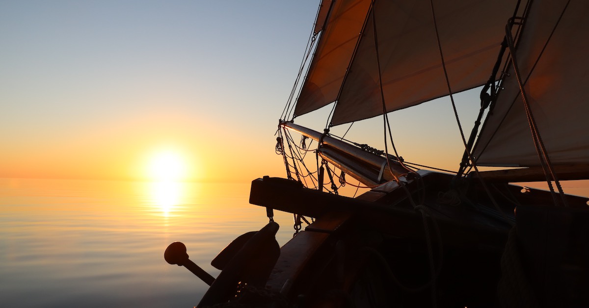 Prow of a boat pointing toward a sunset over the ocean