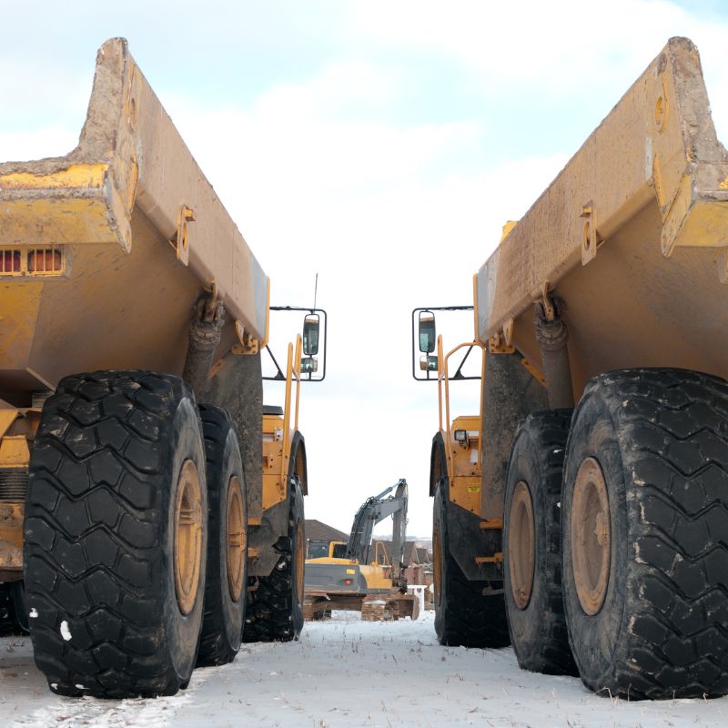 Two yellow articulated dump trucks on snow with a yellow excavator in between them