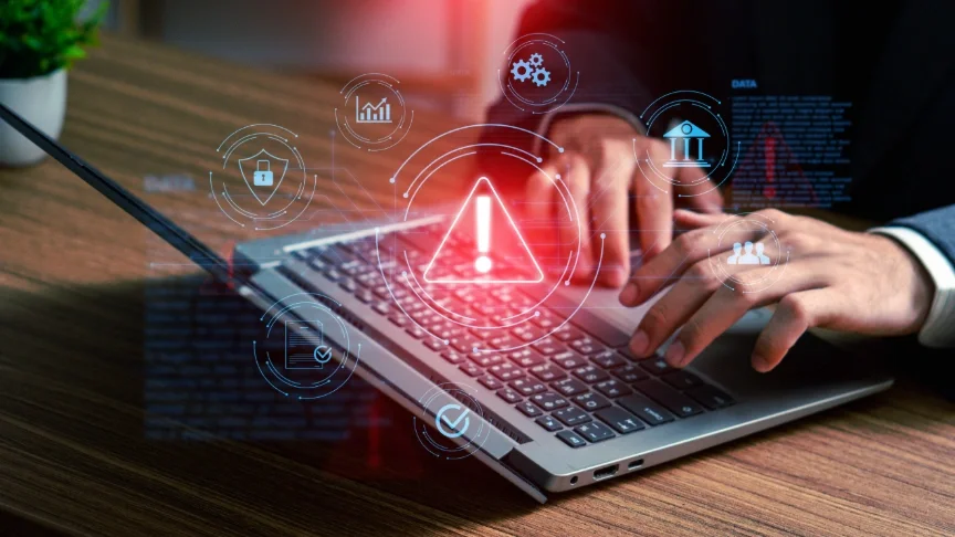man typing on a keybord with a warning sign and other security symbols floating digitally over his hands