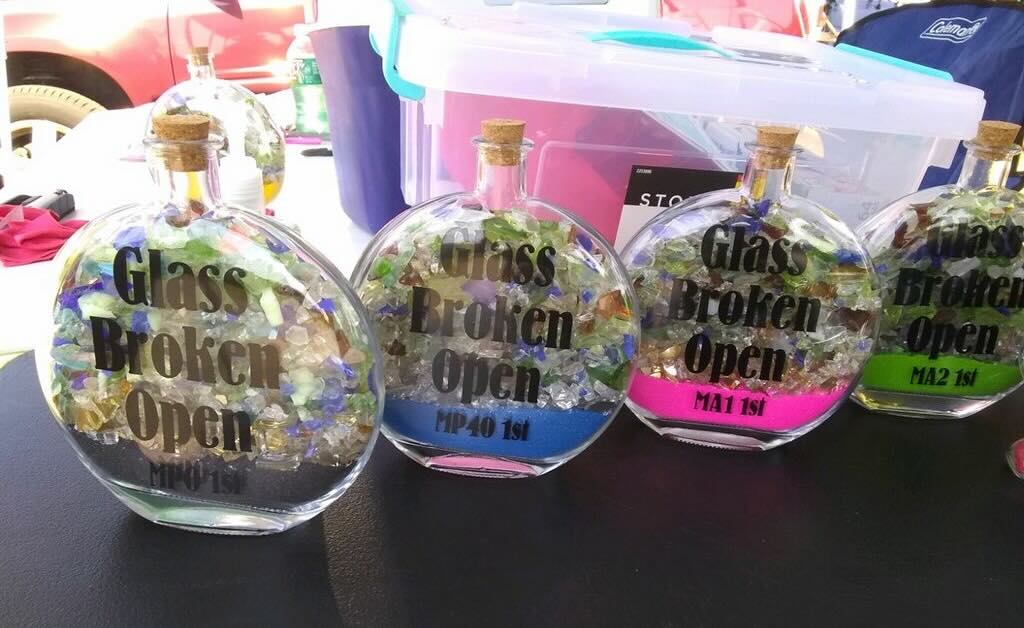 Trophies that are round vials with "Glass Broken Open" printed on them and filled with small shards of colorful glass