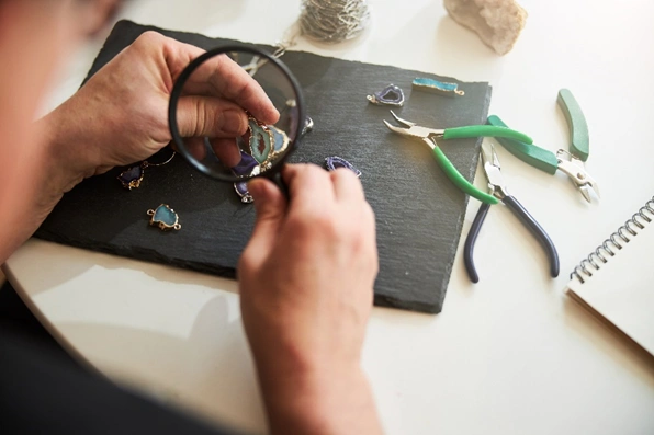 jeweler looking at a piece of jewelry under a magnifying glass with tools around