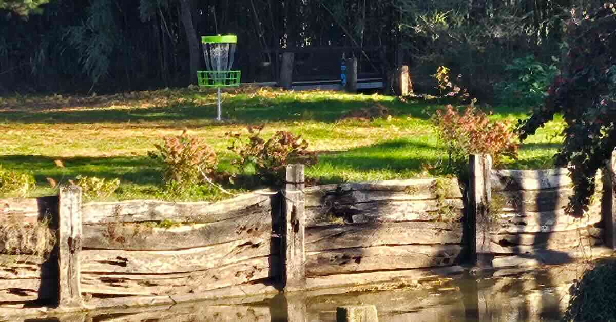 A green disc golf basket on an area elevated above water