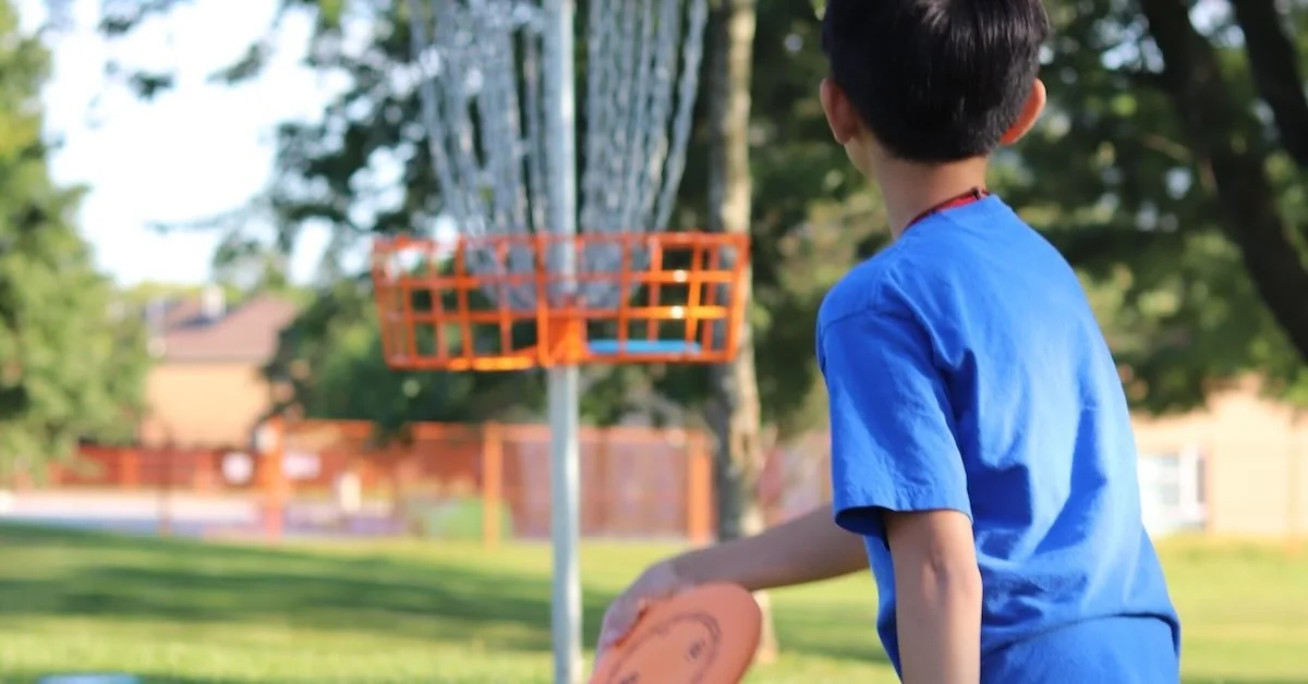 A young boy lines up a put at a disc golf basket