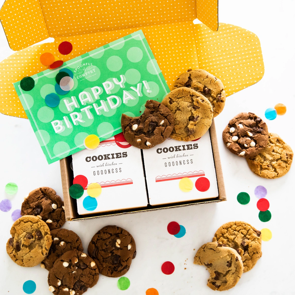 An opened Spoonful of Comfort Birthday Cookie Package, with various cookie flavors and confetti amongst a green card reading, "Happy Birthday!"