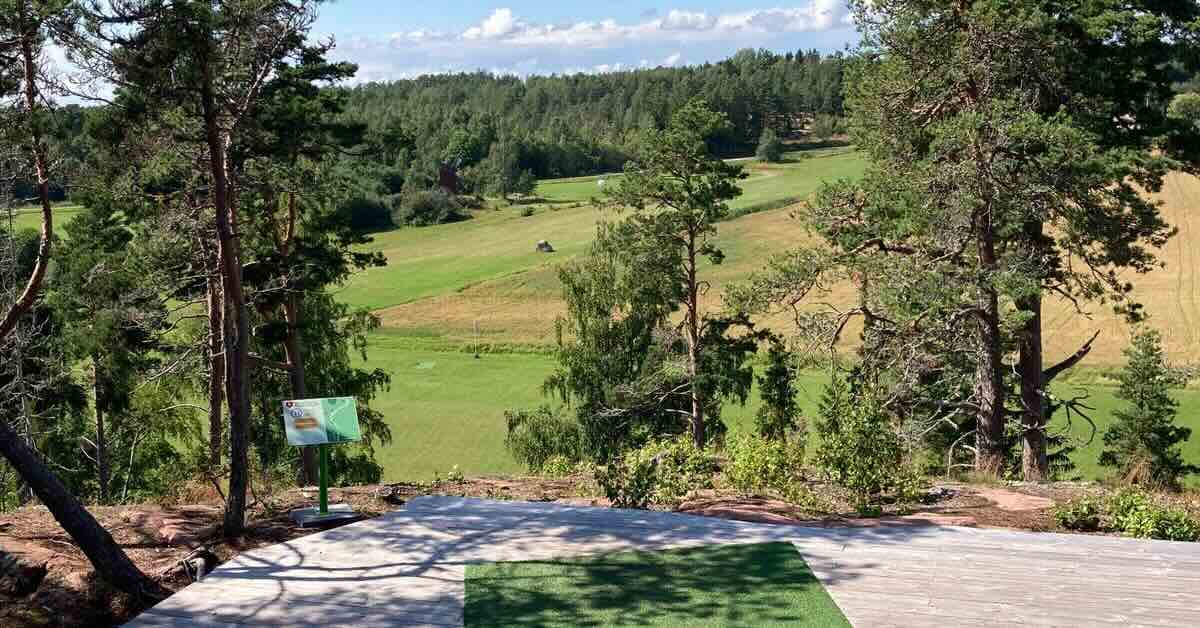 A wooden platform and turf disc golf tee near a big drop-off
