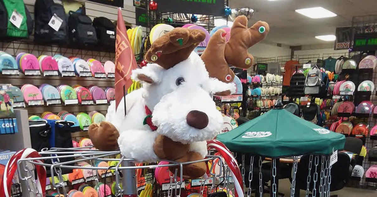 A stuffed white reindeer on top of a disc golf basket with a huge selection of discs organized on shelves in the background