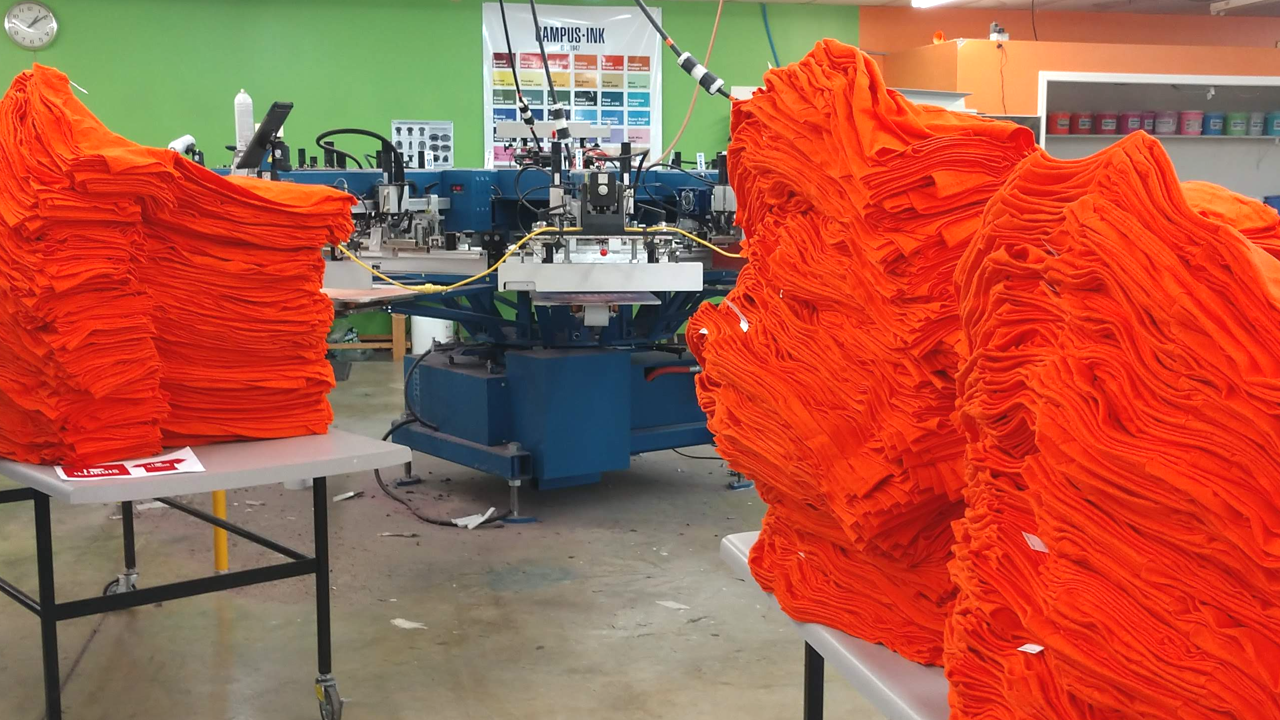 Stacks of orange Next Level shirts waiting to be screen printed.