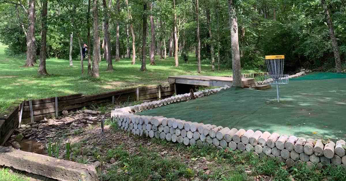 Disc golf basket on a peninsula green surrounded by a creek