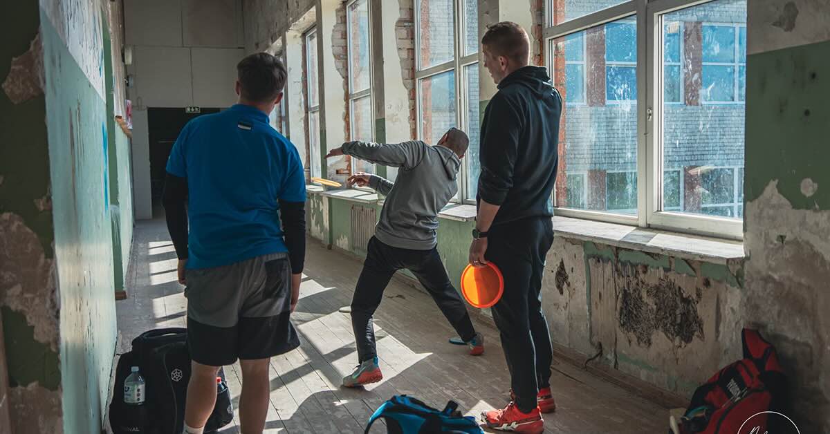 Three men in an old hallway playing disc golf