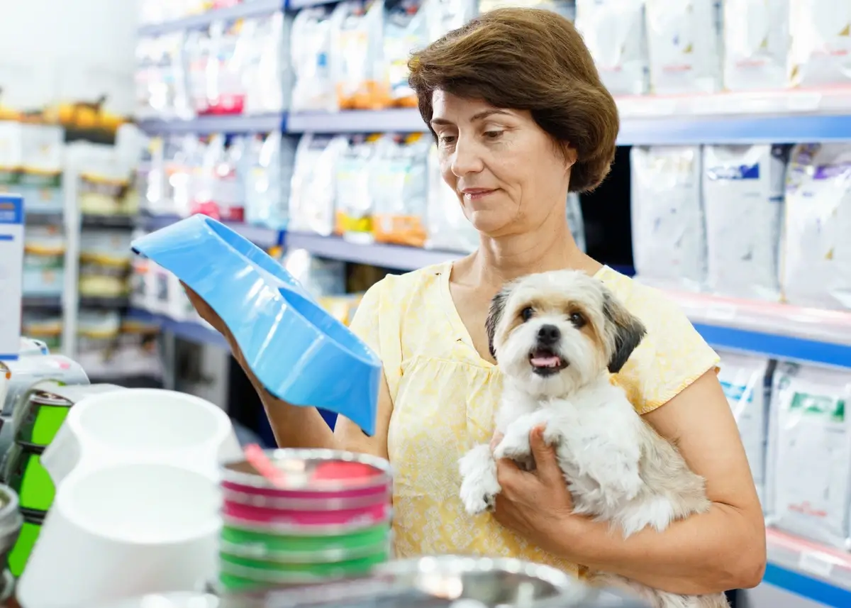 a woman holds a small dog while picking out a dog food bowl