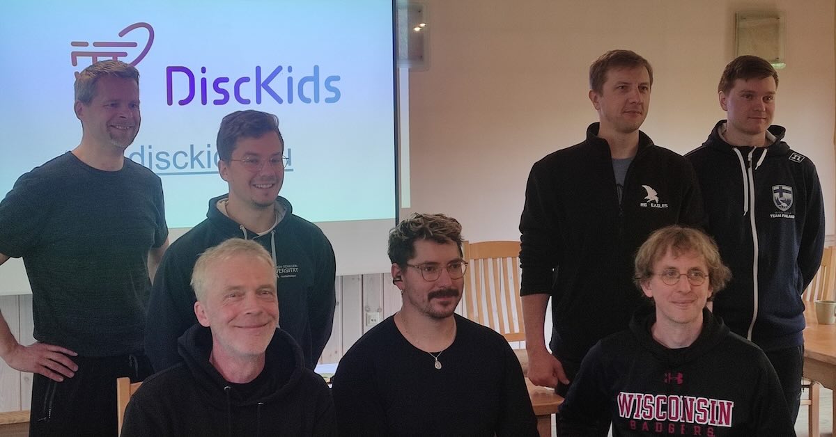 7 men pose for a photo with DISCKids projected on the wall behind