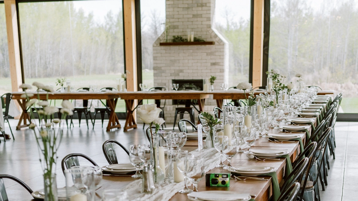Wedding reception tables featuring bud vase with white roses, white table linens and pillar candles.