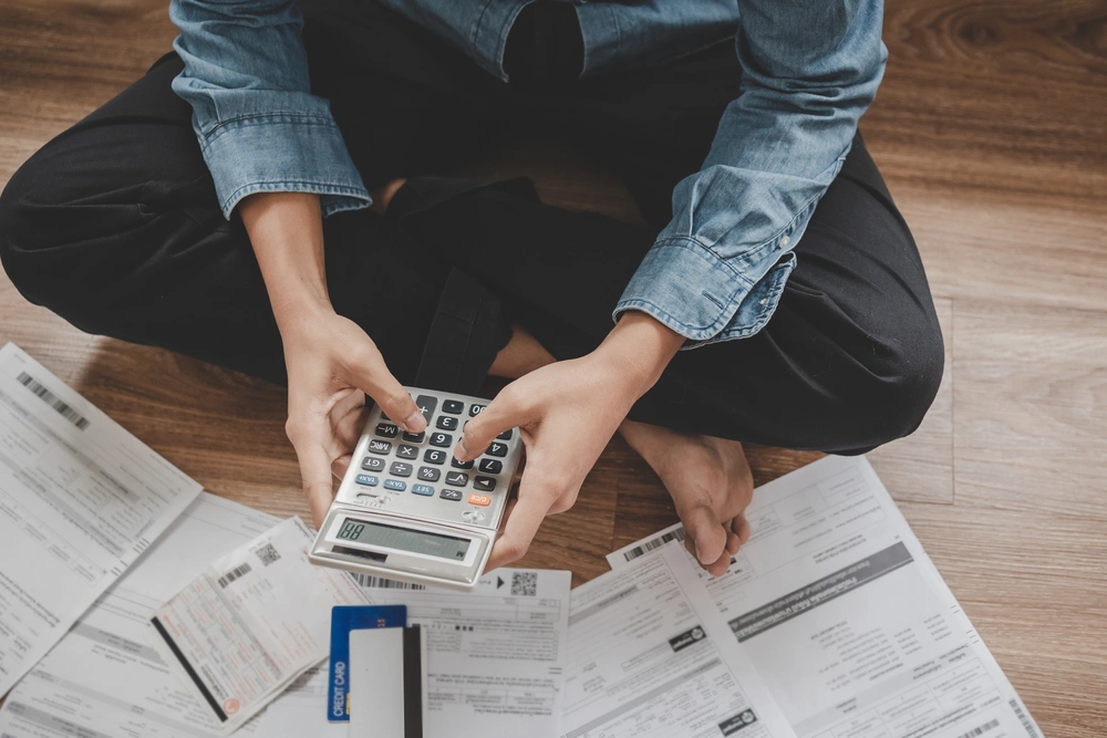 Man sat on the floor holding a calculator and surrounded by paperwork