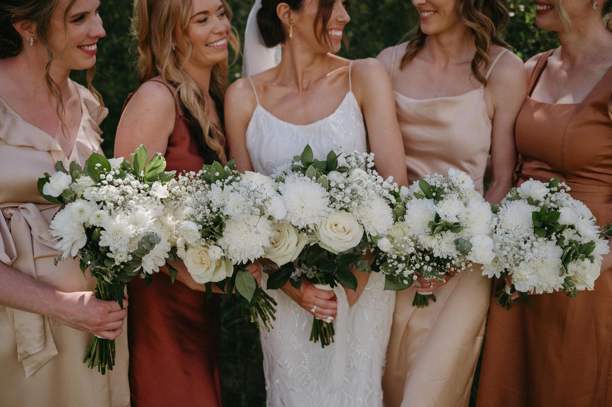 Bride and bridesmaids holding white and green wedding bouquets that feature roses and baby's breath.
