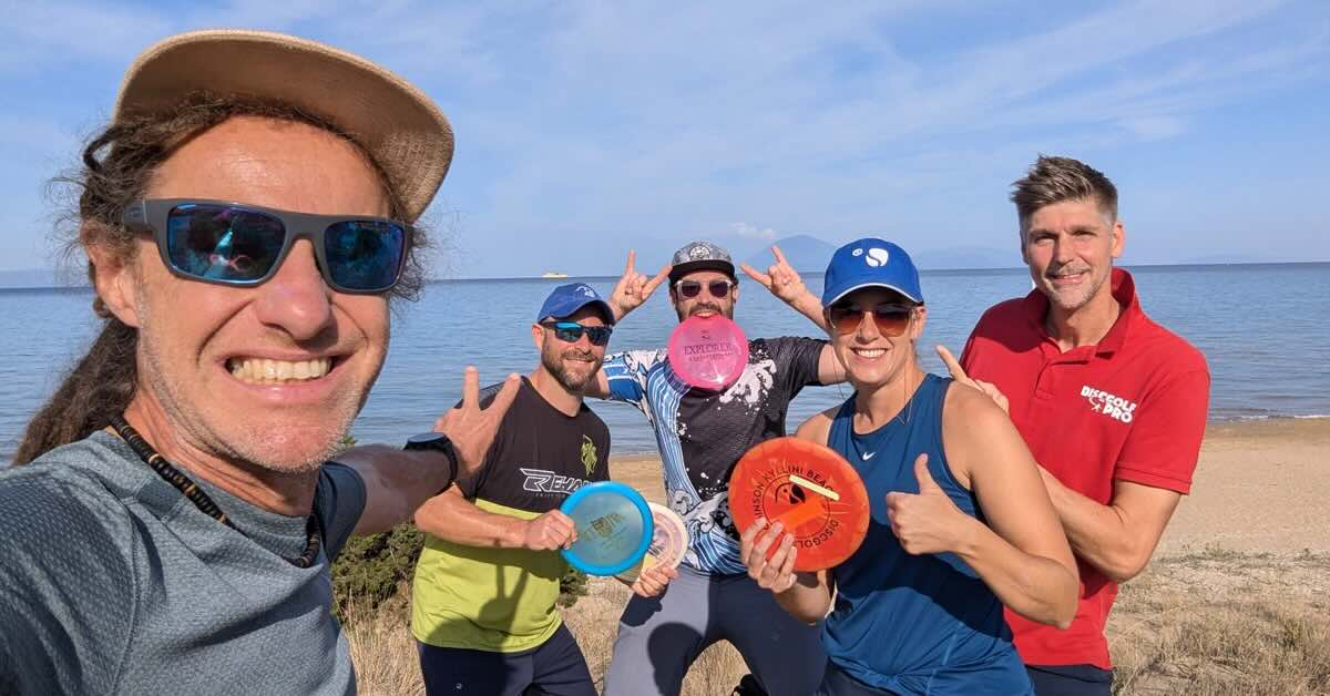 A group photo of people holding discs on a beach