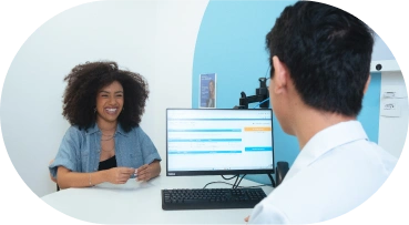 Uma pessoa sorridente sentada de frente para um médico, que também está sentado e mantém uma postura atenta e acolhedora.
