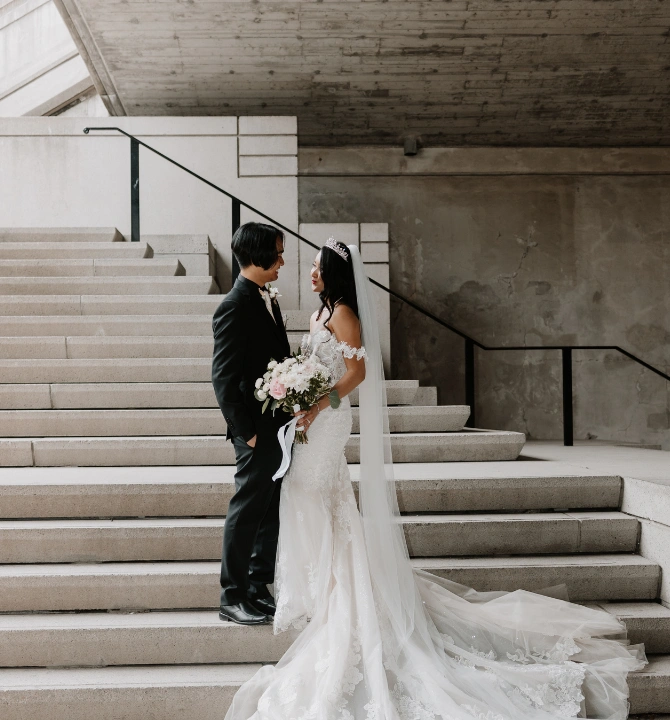 Bride and groom on steps with the bride holding a bridal bouquet and white wedding dress flowing over the steps below.
