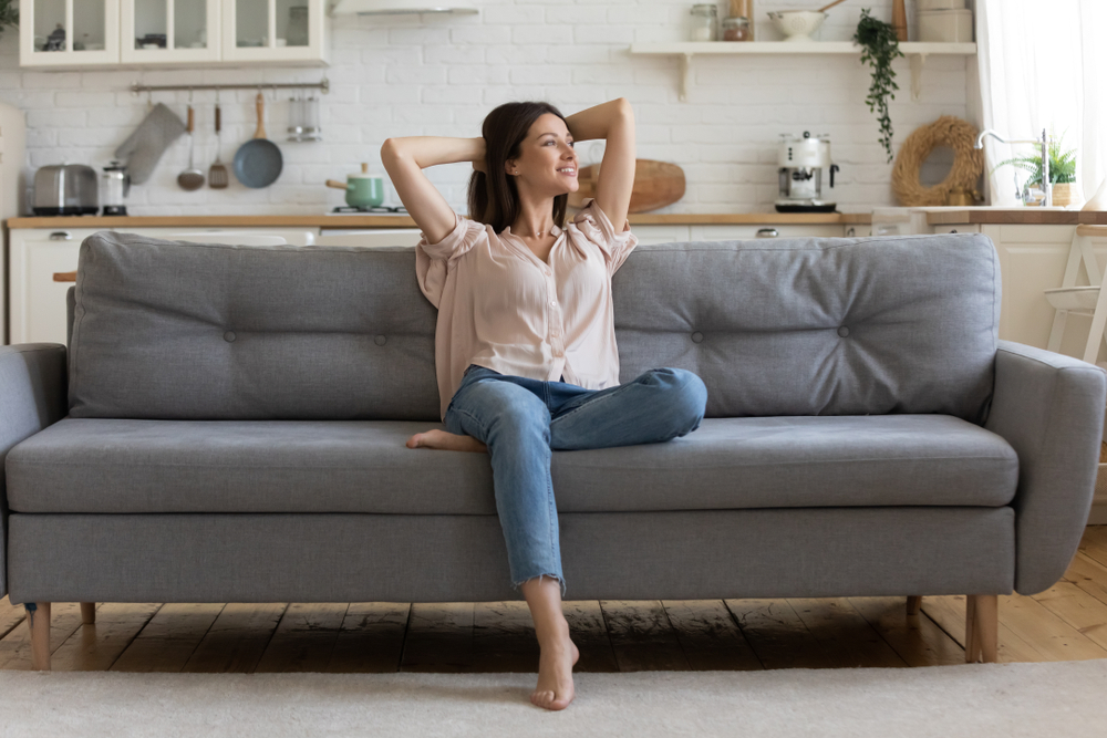 Happy single lady in peach top and jeans sitting on a grey sofa