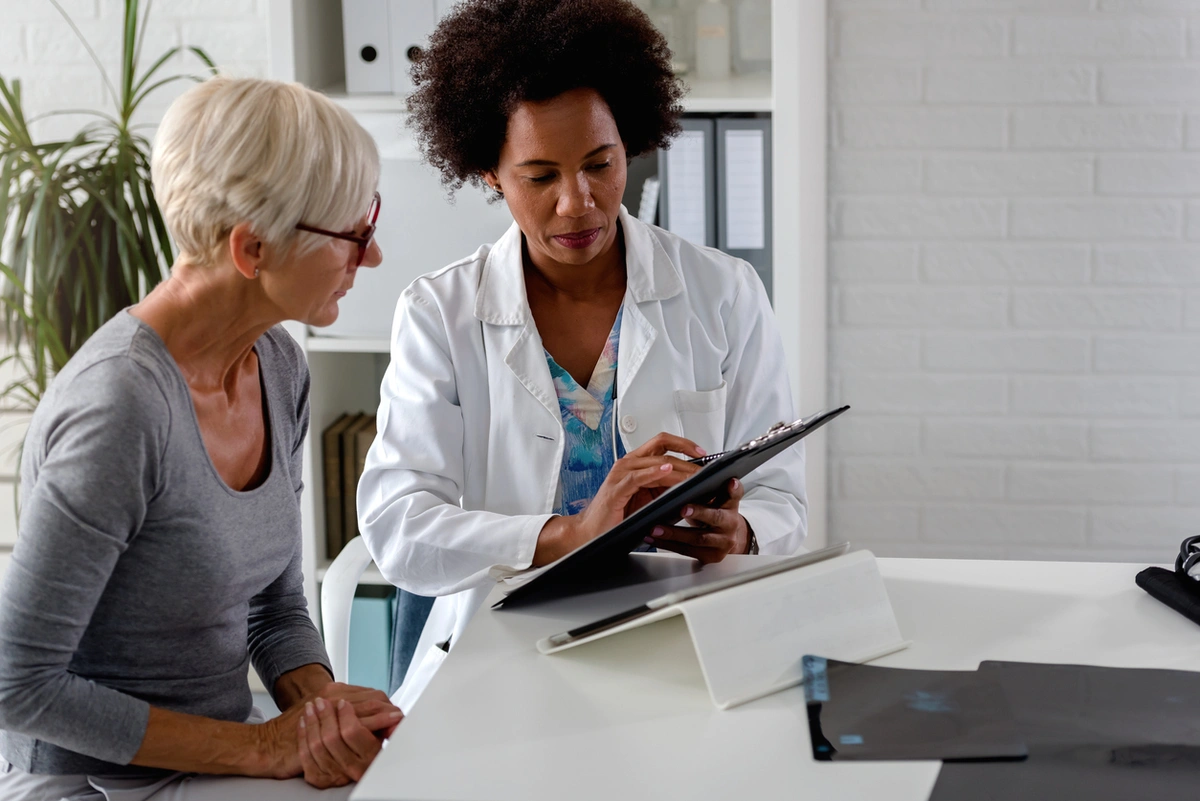 Female doctor sits at desk and chats with an elderly female patient about her test results.