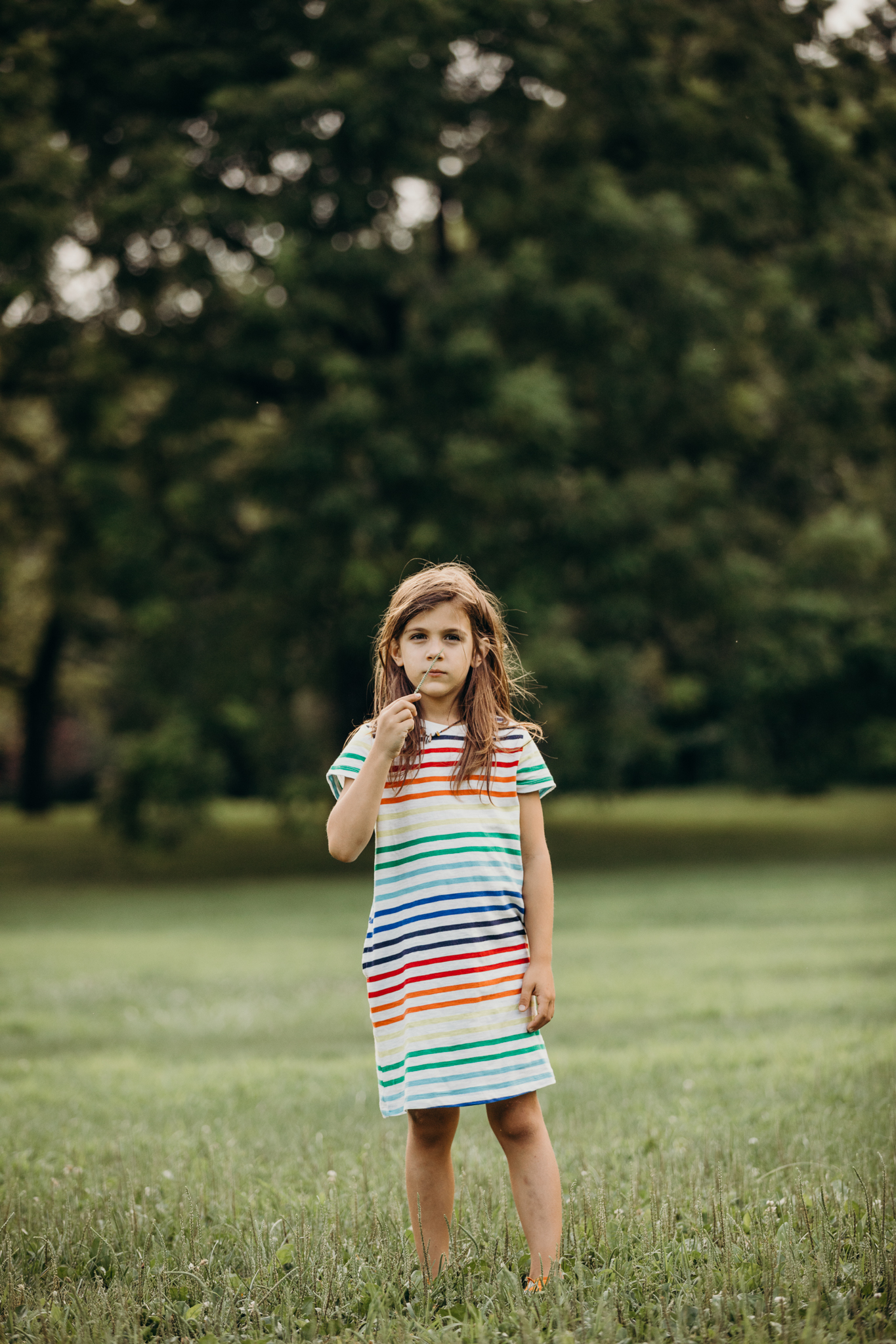 7 year old boy with long hair wearing a rainbow stripe t shirt dress from primary in a park