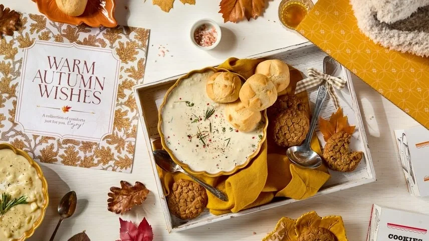 Overhead view of a tray with two bowls of loaded baked potato soup, fresh rolls, cookies, and a metal ladle with a gingham ribbon, with one bowl on a tray.