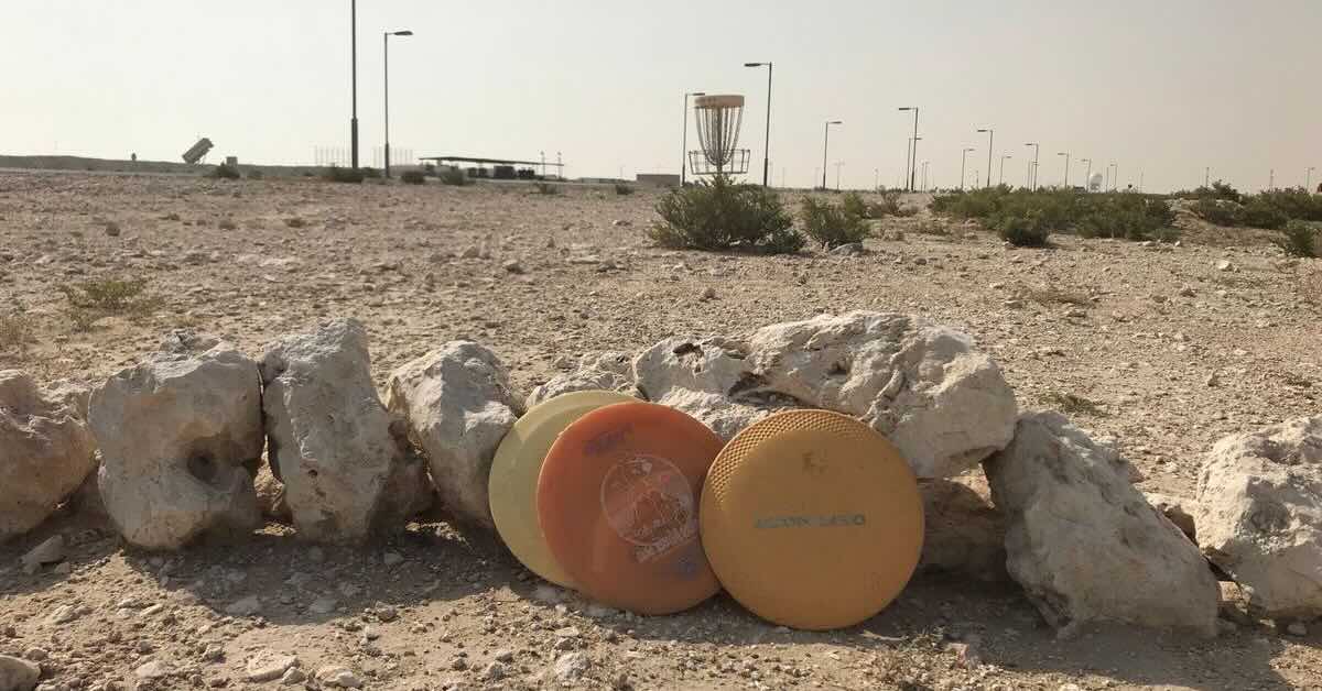 Disc golf discs leaning on rocks in a desert landscape with a basket in the background