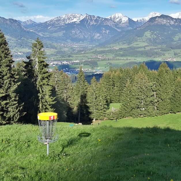 A disc golf basket with a stunning view of the Alps behind