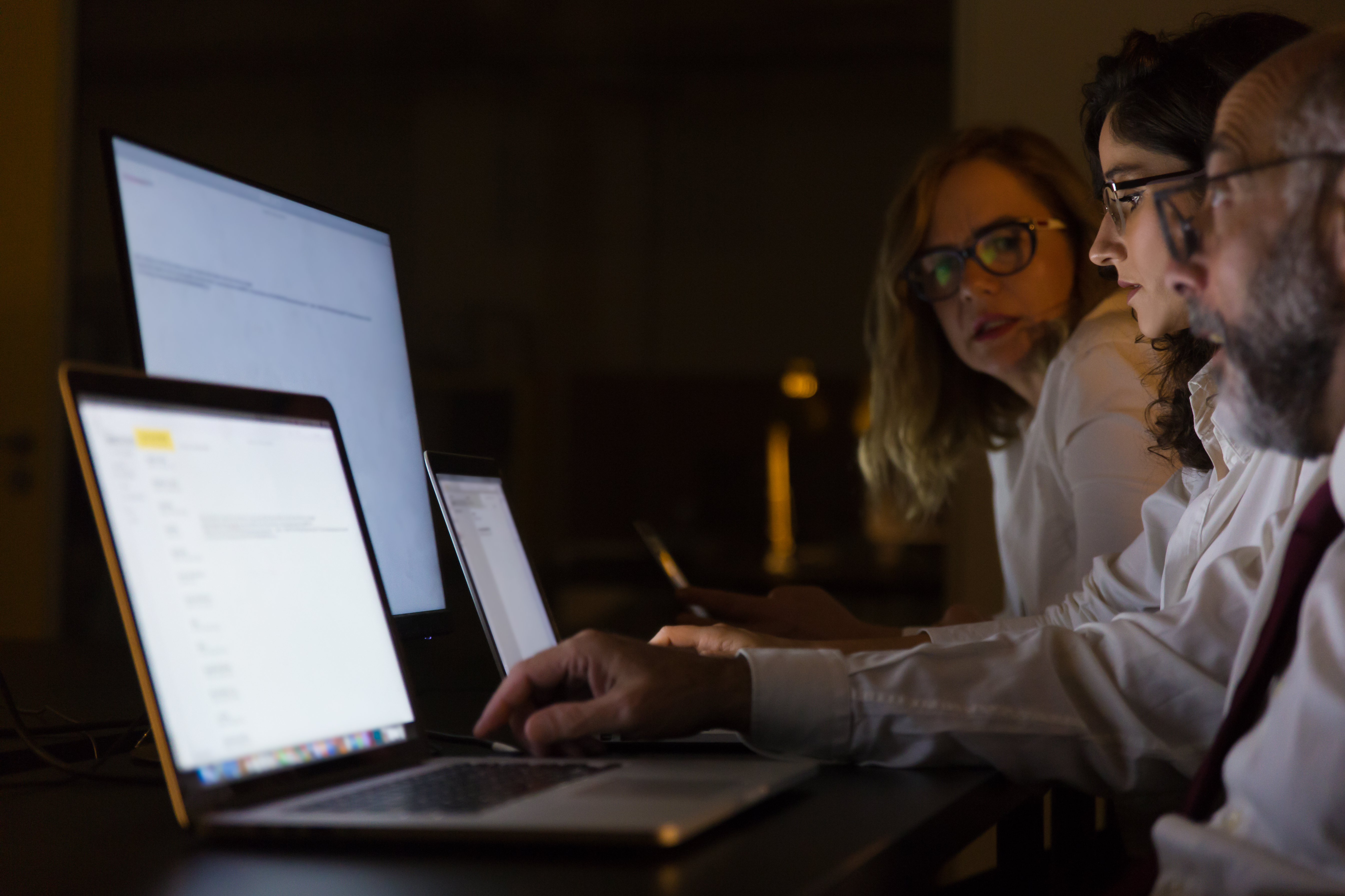Business colleagues working late at night on their laptops in a dimly lit office.