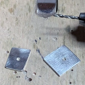 two squares of silver metal with a hole in the center of each for a rivet