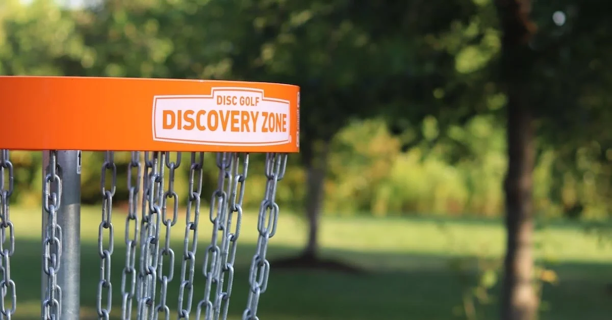 An orange disc golf basket band with "disc golf discovery zone" in white at its center