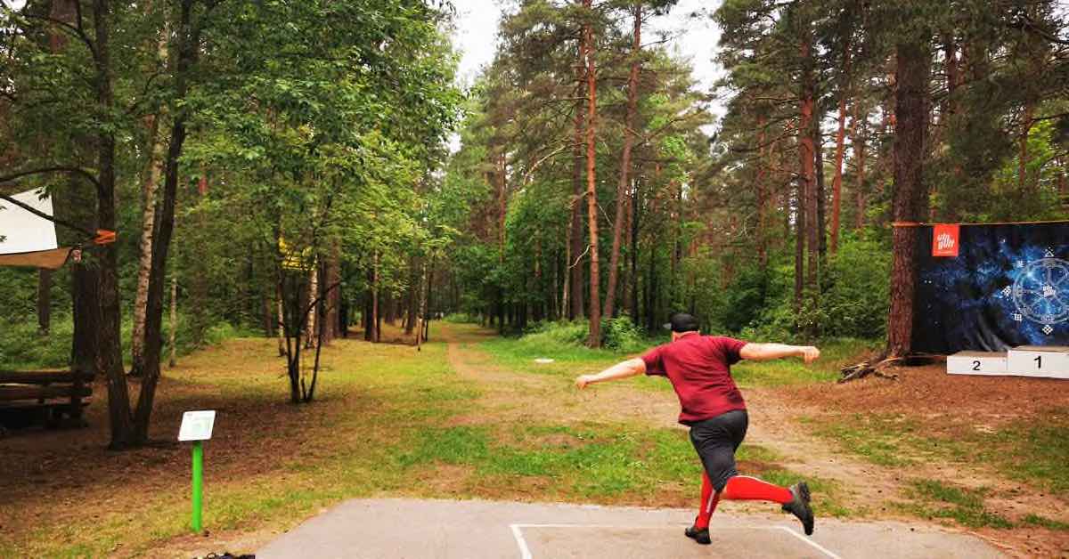 person throwing from a tee pad on a wooded disc golf fairway