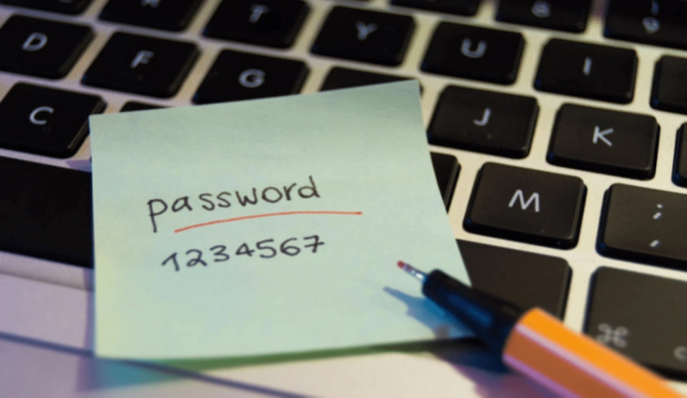 the words "password" and "1234567" are written in pen on a green sticky-note, resting on a computer keyboard.