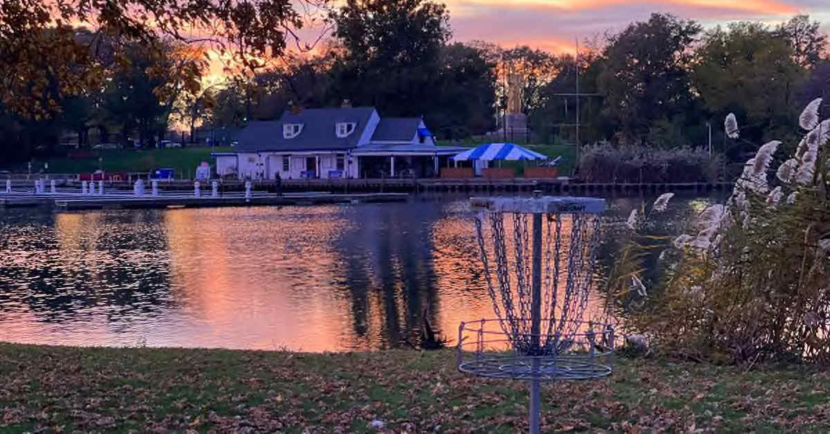 A disc golf basket in front of water at sunset