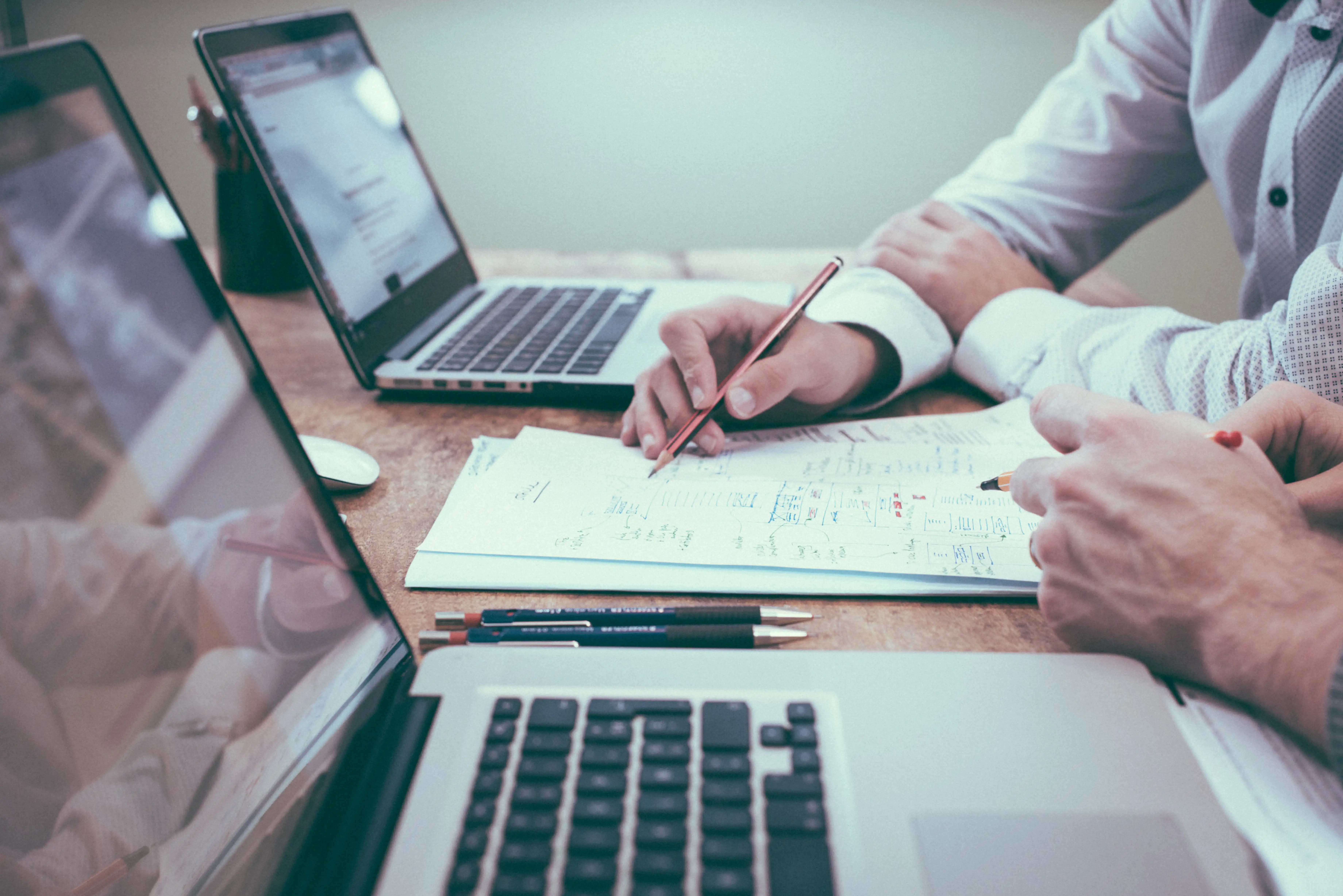 A business owner and a consultant from a software development company discuss a new custom CRM development project at a desk.