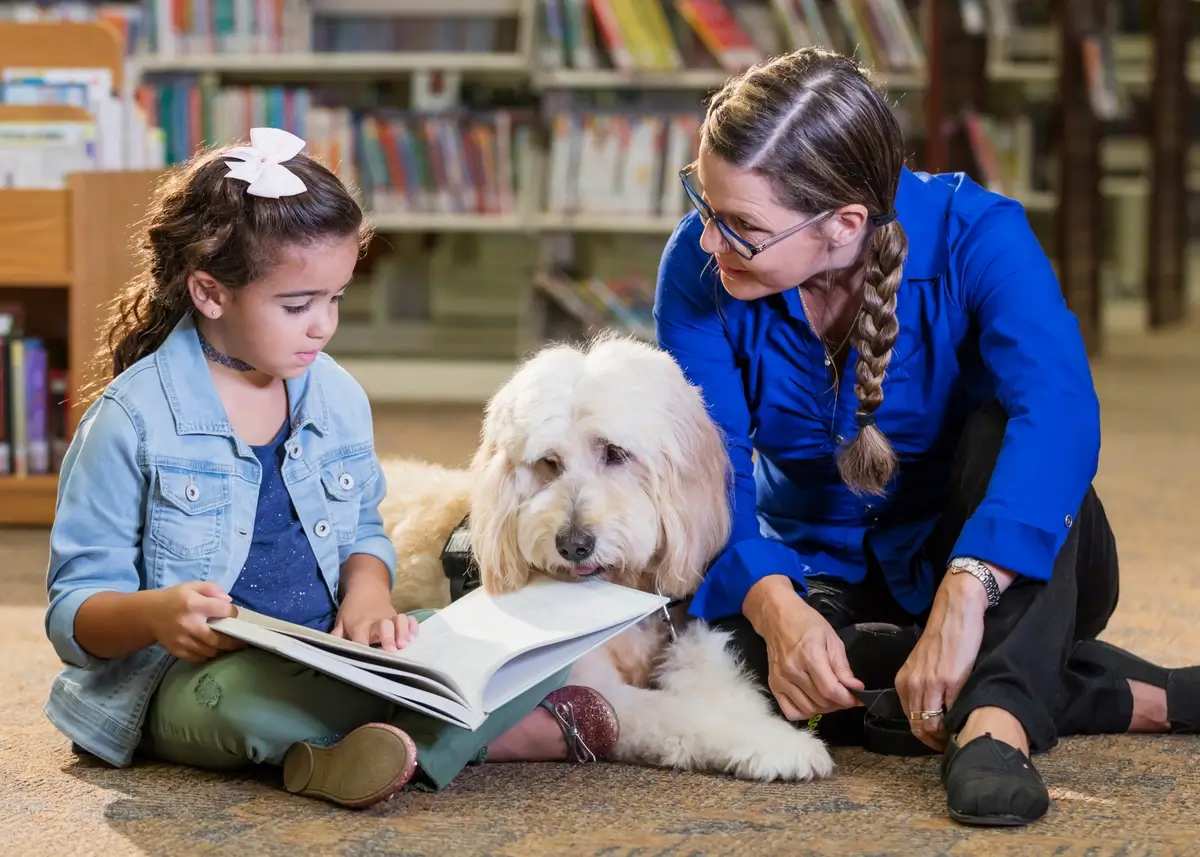 a girl reads to a dog and an adult woman