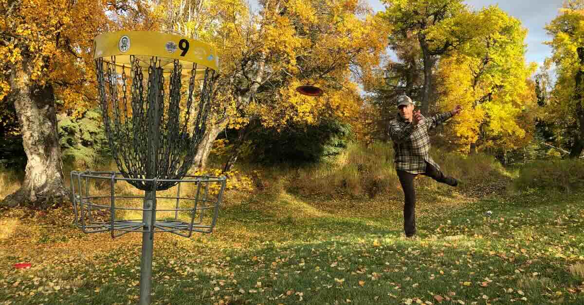 A man putts at a yellow disc golf basket in a landscape of trees in fall yellow