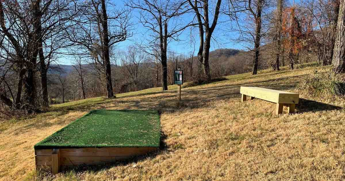 A turf disc golf tee pad at a mountainous course with bare trees on a sunny winter day