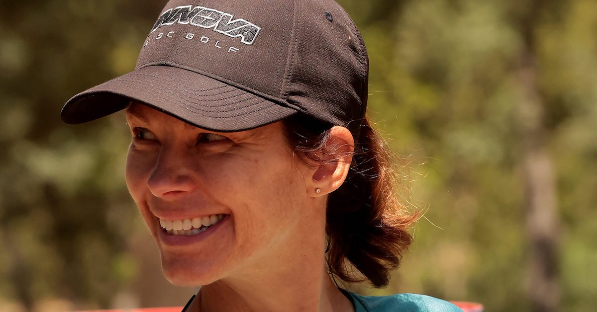 A woman outdoors in a baseball cap smiles