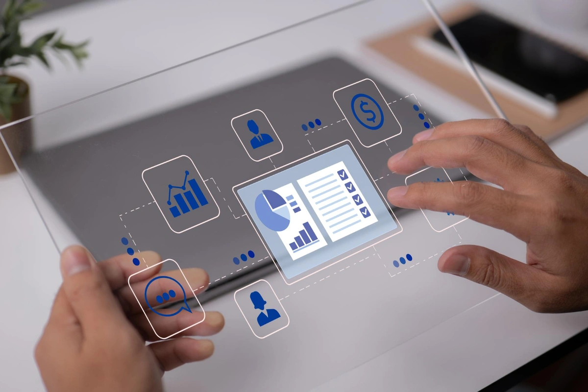 A person's hands interact with a futuristic transparent touch screen displaying various business analytics graphs and icons. It suggests a concept of advanced technology integrated with digital analytics and user interfaces.