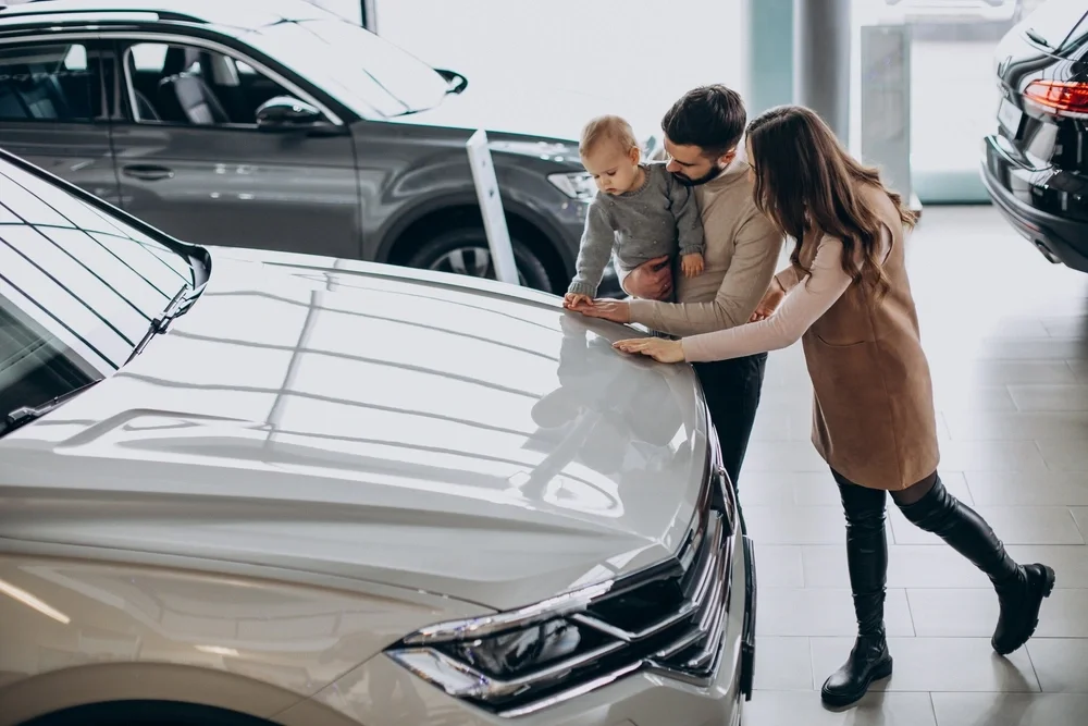 A young couple and their small child, looking at a used car in a dealership.