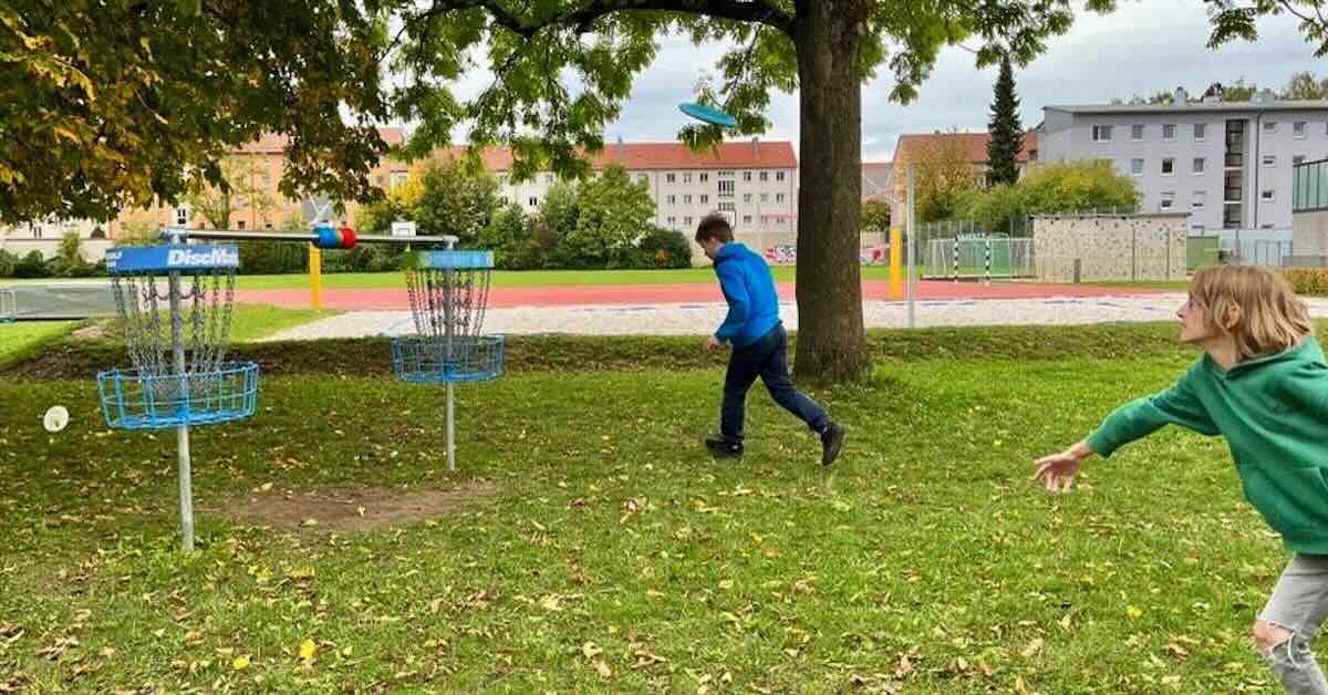 Two boys throwing at two disc golf baskets set up with scoring rings in the middle