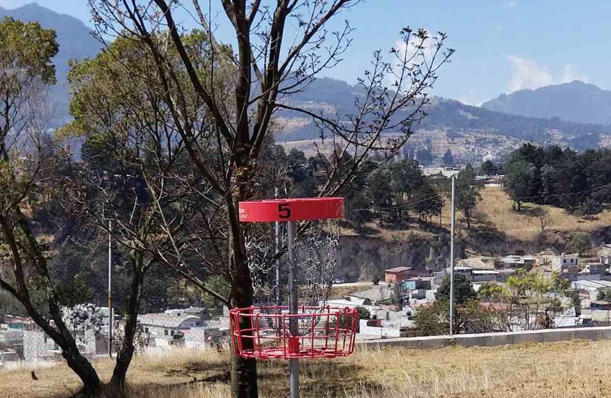 A red-banded disc golf basket with mountains in the background