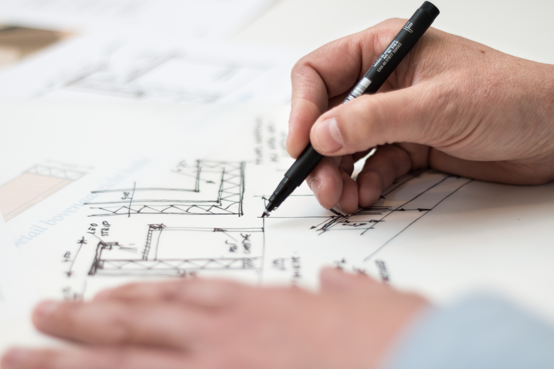 Hands drawing an architectural plan with a black pen