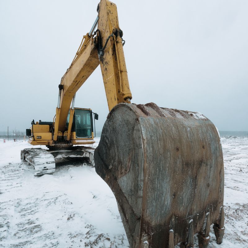 Yellow excavator with a bucket attachment on a snow covered lot with snow on its tracks