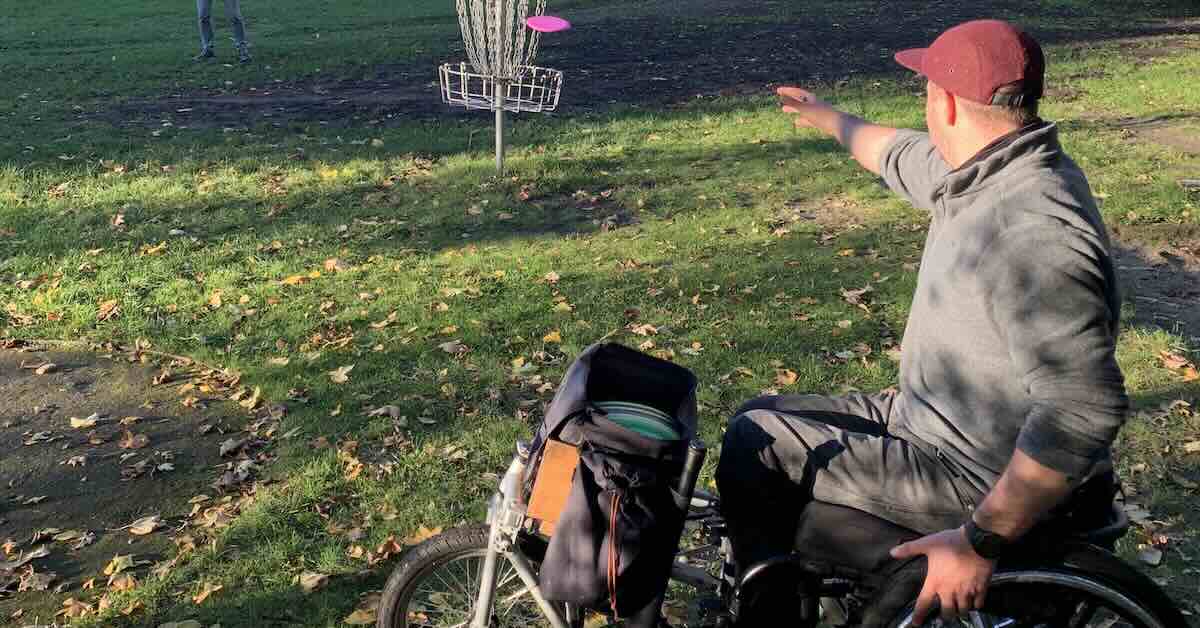 A person in a wheelchair throws a disc golf putt at a basket